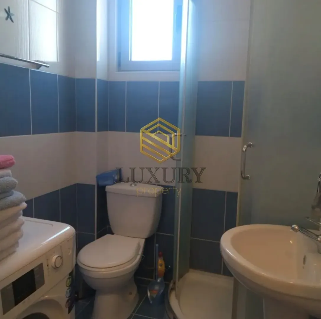 Small bathroom with blue and white tiles, toilet, sink, and shower cabin.