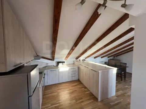 Attic kitchen with wooden ceiling beams and a dining area in the background. - image 14