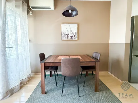 Dining area with a wooden table and chairs, located next to a window with light curtains. - image 4