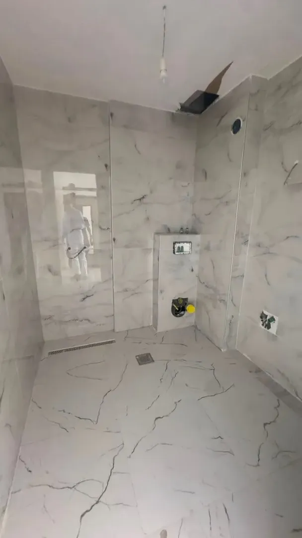 Nekorišćeno kupatilo sa mermernim pločicama i ugradnim instalacijama.