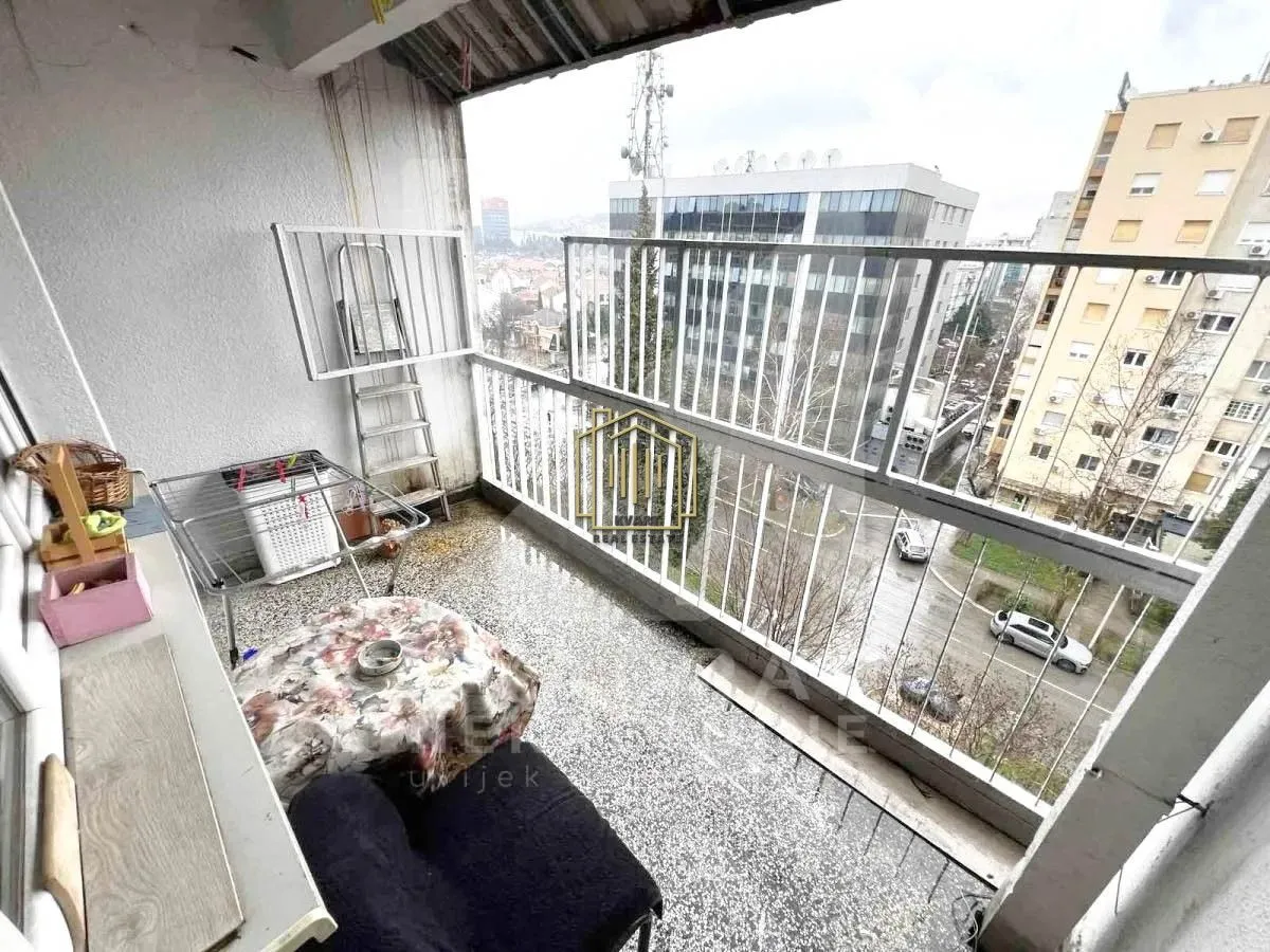 Natkriveni balkon sa metalnom ogradom i pogledom na grad.