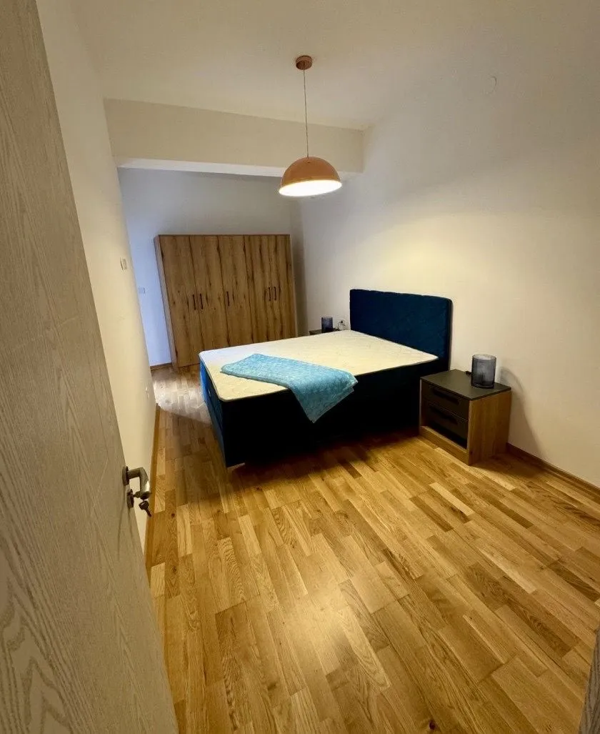 Spavaća soba sa bračnim krevetom, plakarom i drvenim podom.