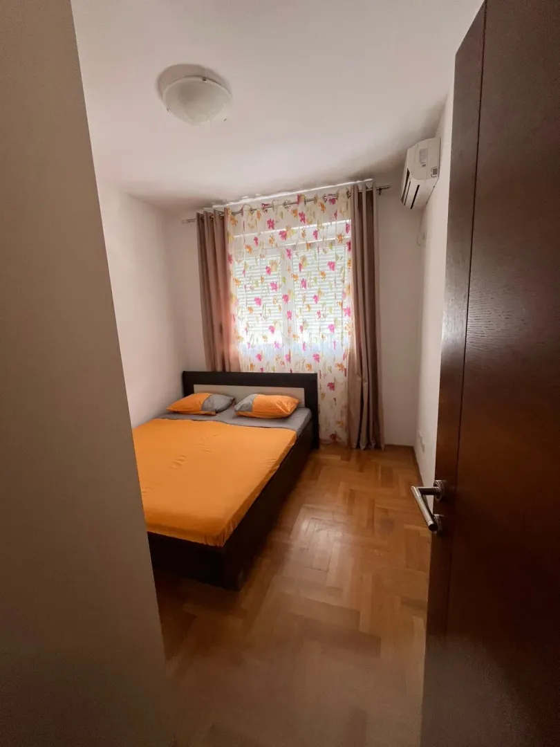 Small bedroom with a double bed, parquet flooring, and a window with curtains.