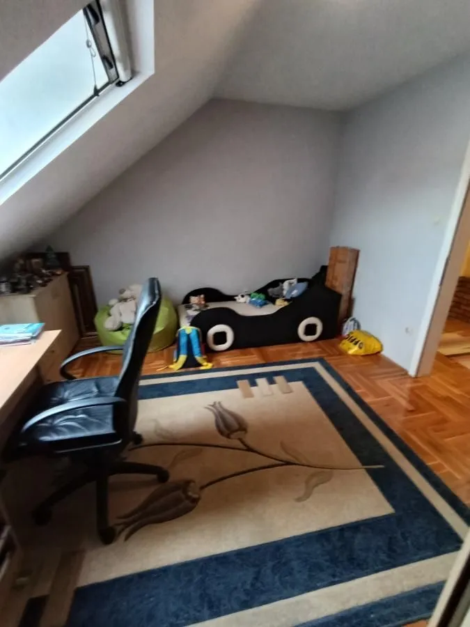 Dečja soba u potkrovlju sa krevetom u obliku automobila i radnim stolom.