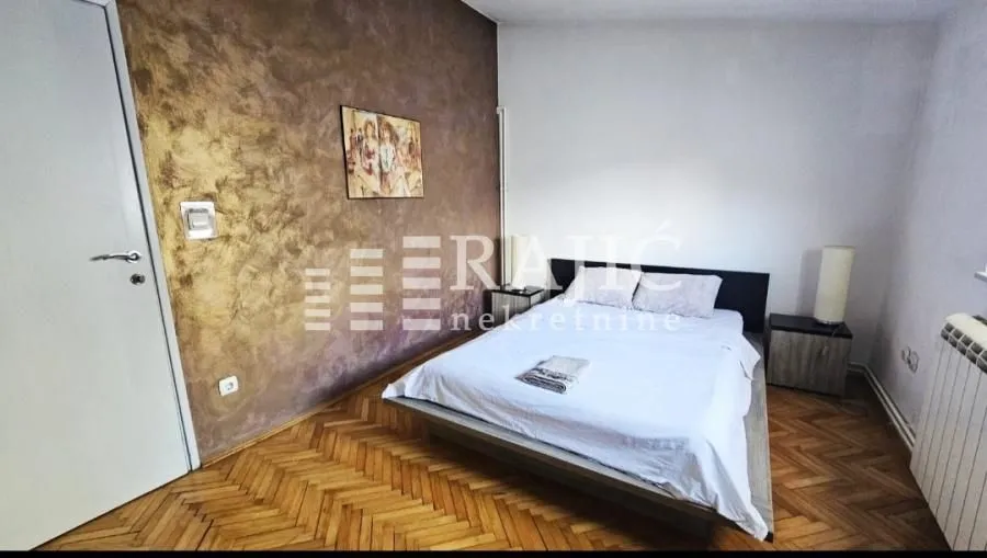 Bedroom with a double bed, parquet flooring, and a decorative wall.
