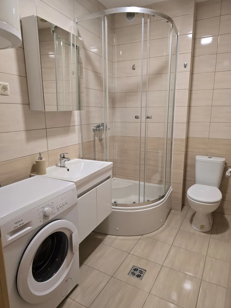 Moderno opremljeno kupatilo sa tuš kabinom i veš mašinom.