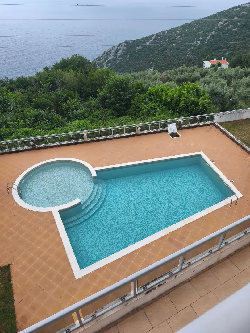 Pogled odozgo na bazen i okolno zelenilo sa morem u pozadini.