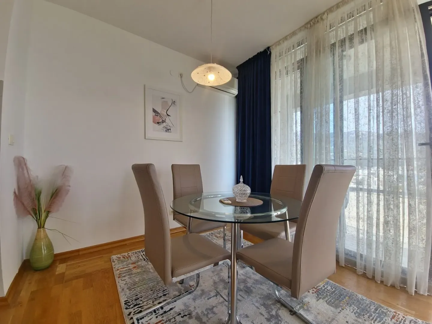 Dining area with a round glass table and four chairs by the window.