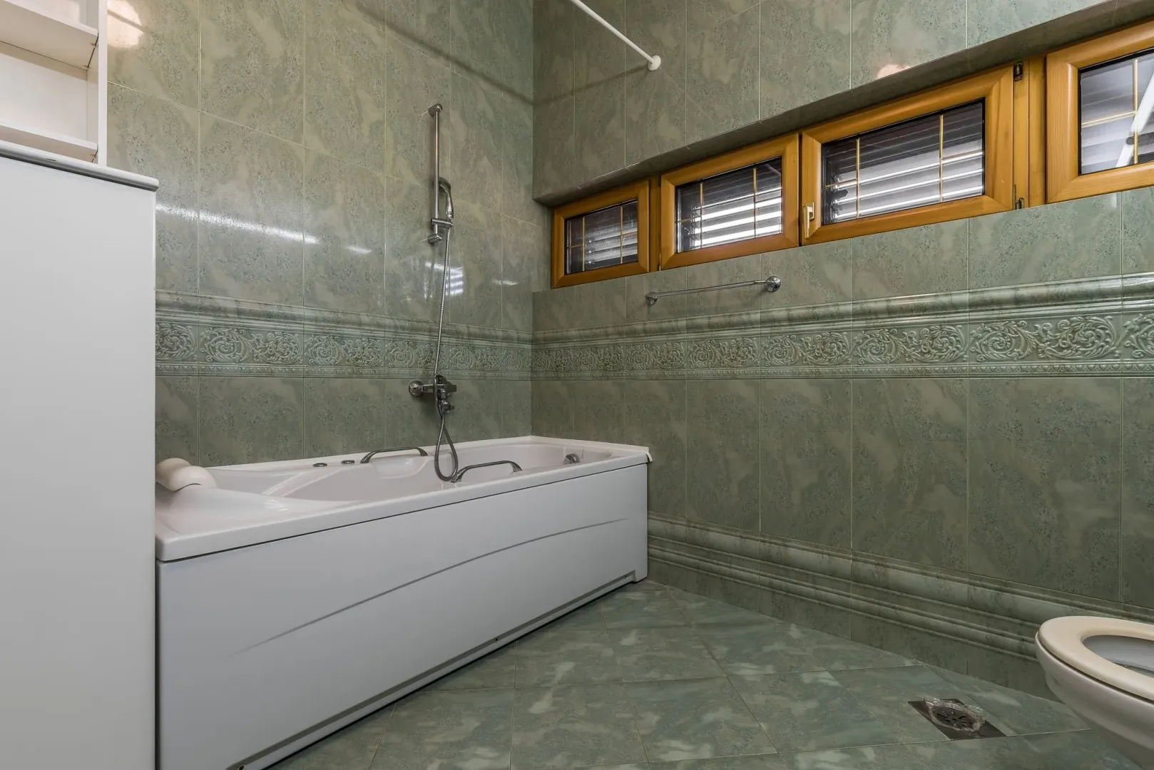 A bathroom featuring green wall tiles and a bathtub.