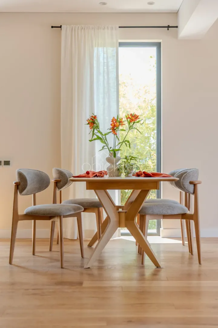 Dining table with four chairs and decorative flowers in front of the window.