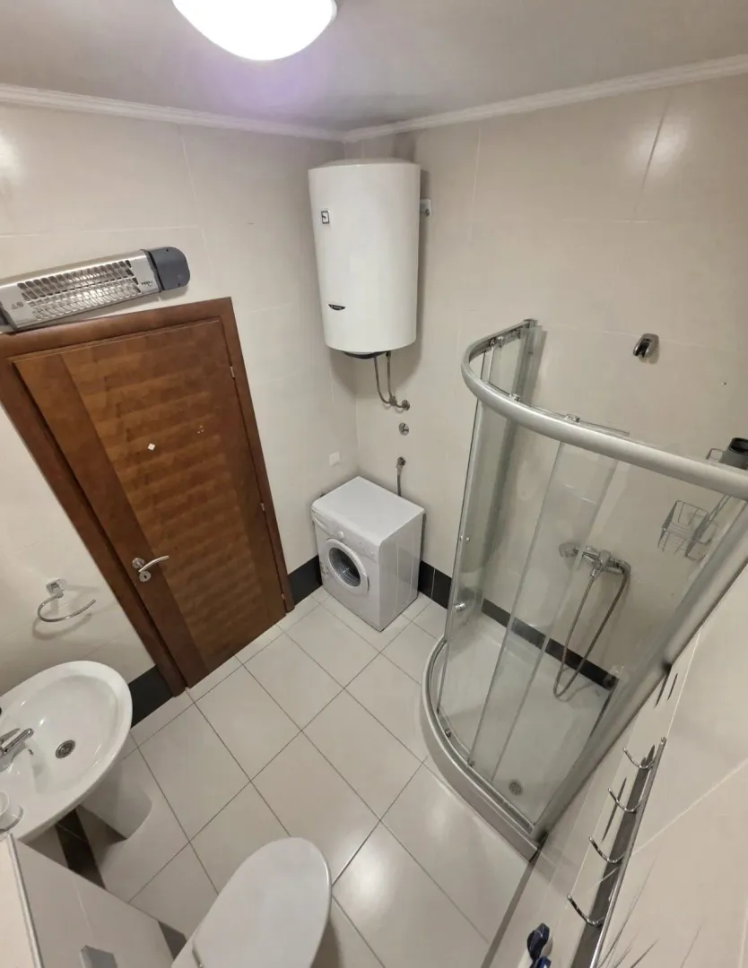 Manje kupatilo sa tuš kabinom, umivaonikom, WC šoljom i veš mašinom.