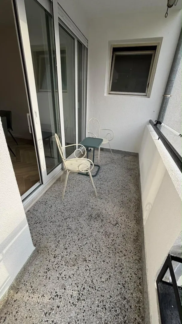 Small narrow balcony with seating furniture and glass sliding doors.