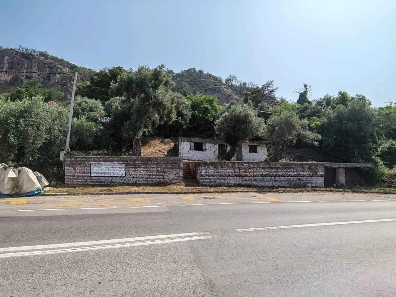 Pogled sa puta na plac sa starom kućom i drvećem.