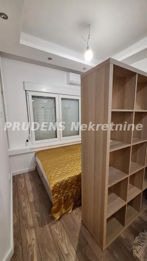 Manja spavaća soba sa krevetom i pregradnom drvenom policom.
