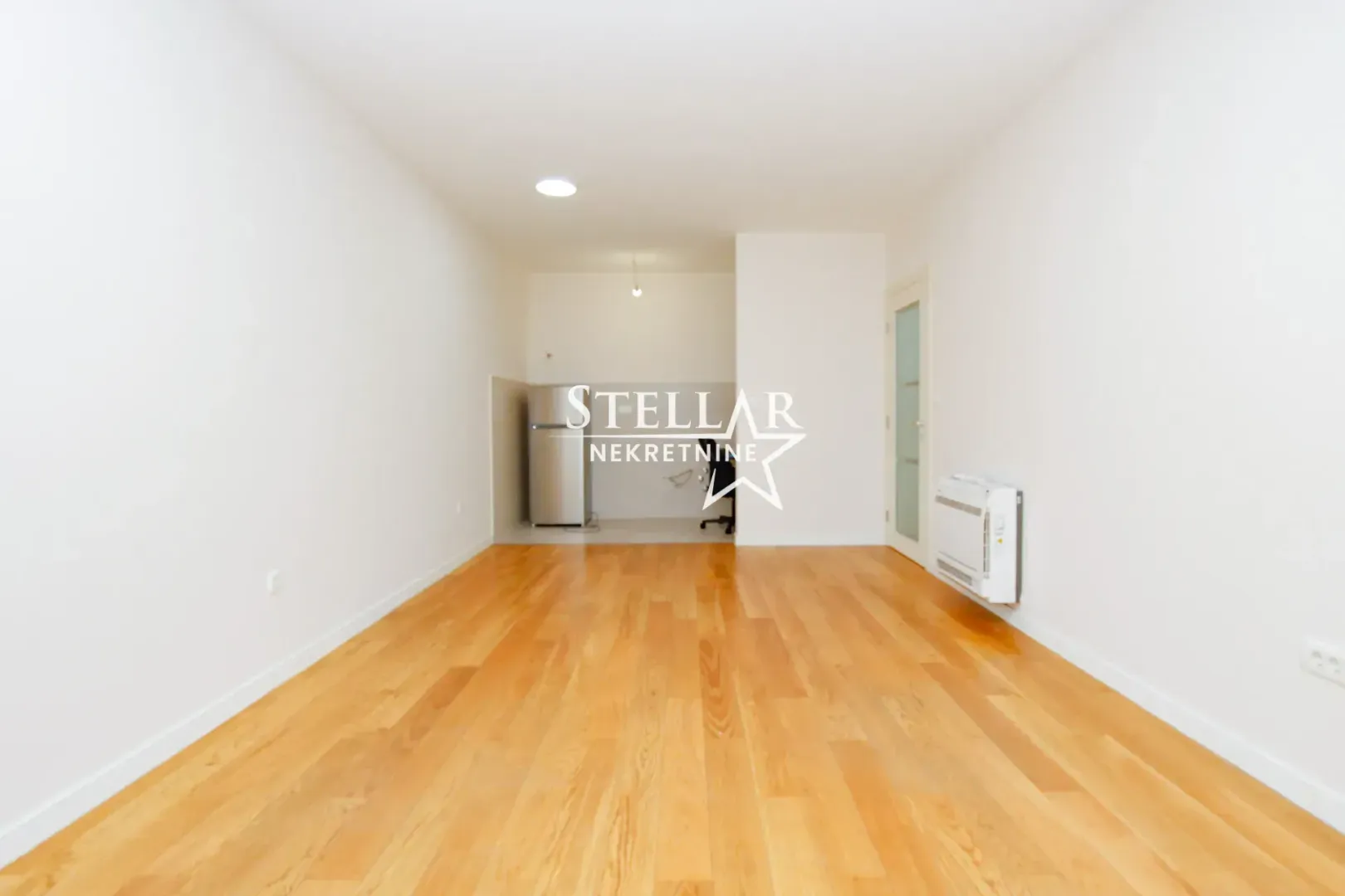 Empty living room with wooden flooring and white walls.