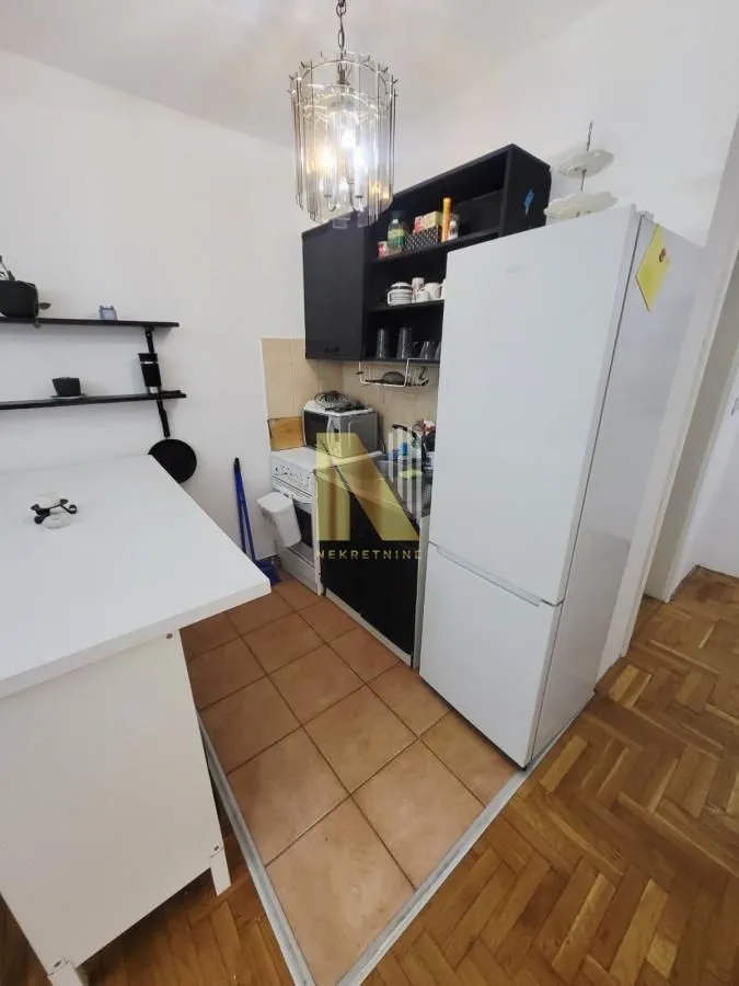 Manja kuhinja sa belim frižiderom i crnim kuhinjskim elementima.
