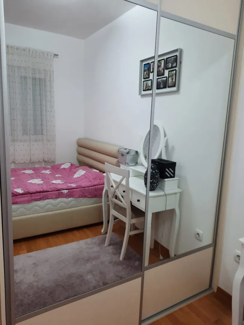 Namještena spavaća soba sa bračnim krevetom, radnim stolom i velikim ogledalom.