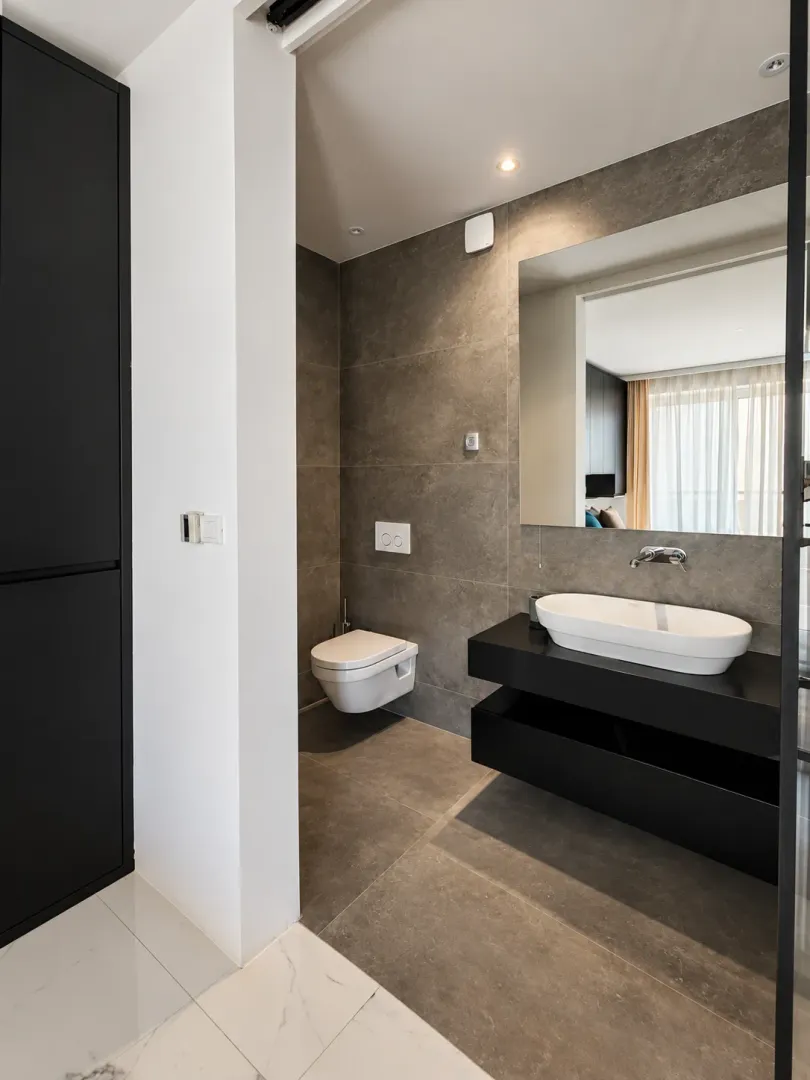 Modern bathroom with a sink and toilet in gray and black tones.