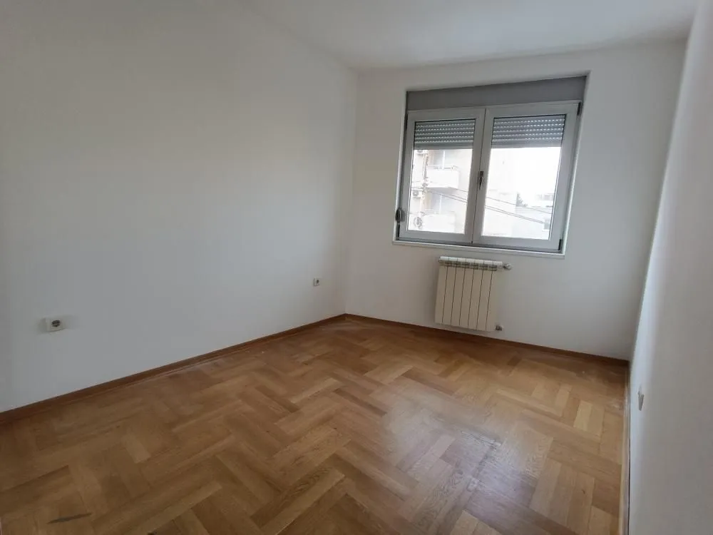 Prazna soba sa parketom i prozorom.