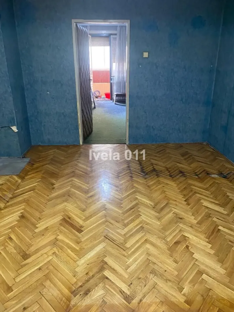Prazna soba sa parketom i plavim zidovima sa pogledom na drugu prostoriju.