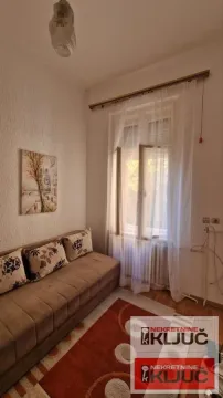 Manja dnevna soba sa kaučem, tepihom i prozorom sa zavesama. - image 2