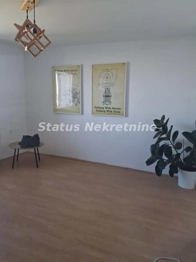 Dnevna soba sa drvenim podom, modernim lusterom i slikama na zidu.
