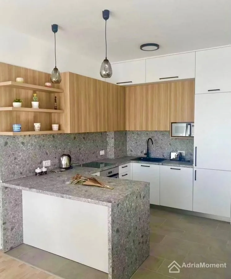 Moderna kuhinja sa drvenim elementima, bijelim ormarićima i radnom površinom od granita.