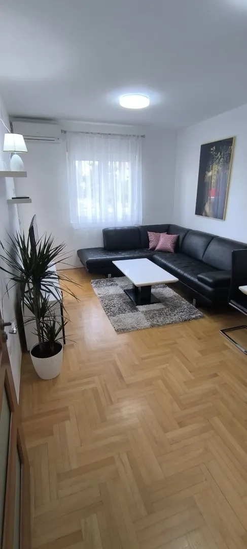 Bright living room with a black corner sofa and parquet flooring.