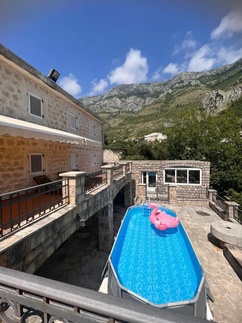 Pogled na dvorište kuće sa bazenom i planinskim pejzažom u pozadini.