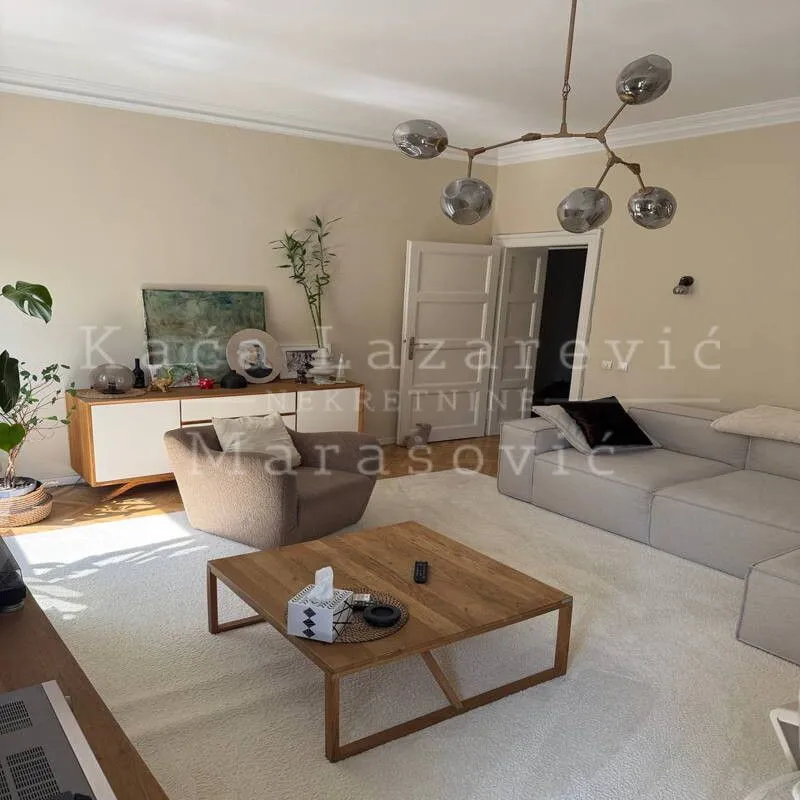 Prostrana dnevna soba sa garniturom, drvenim stočićem i modernim lusterom.