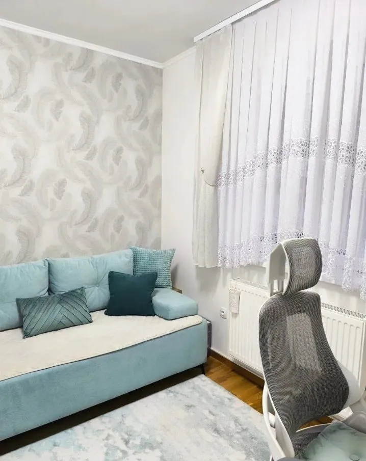 Manja svetla dnevna soba sa tirkiznim trosedom i radnom stolicom.