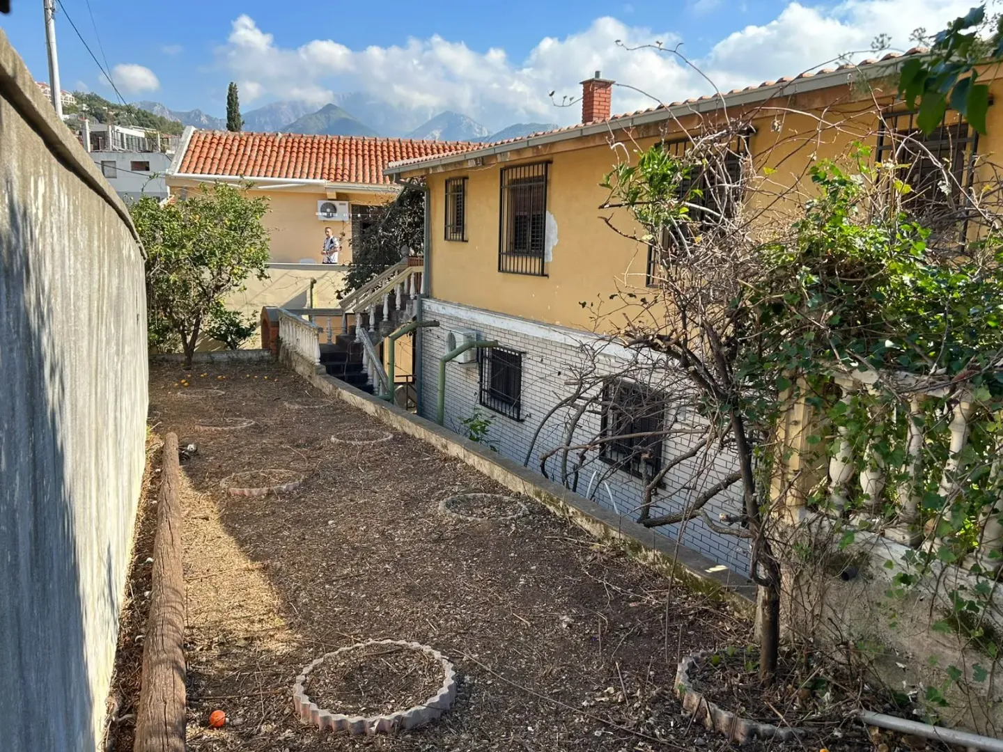 Pogled na dvorište i spoljašnost kuće sa planinama u pozadini.