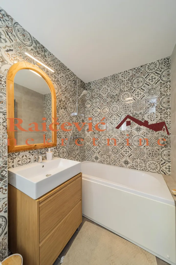 Bathroom equipped with a washbasin, mirror, and bathtub featuring decorative tiles.