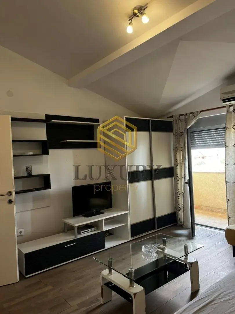 Namještena dnevna soba sa TV komodom i izlazom na terasu.
