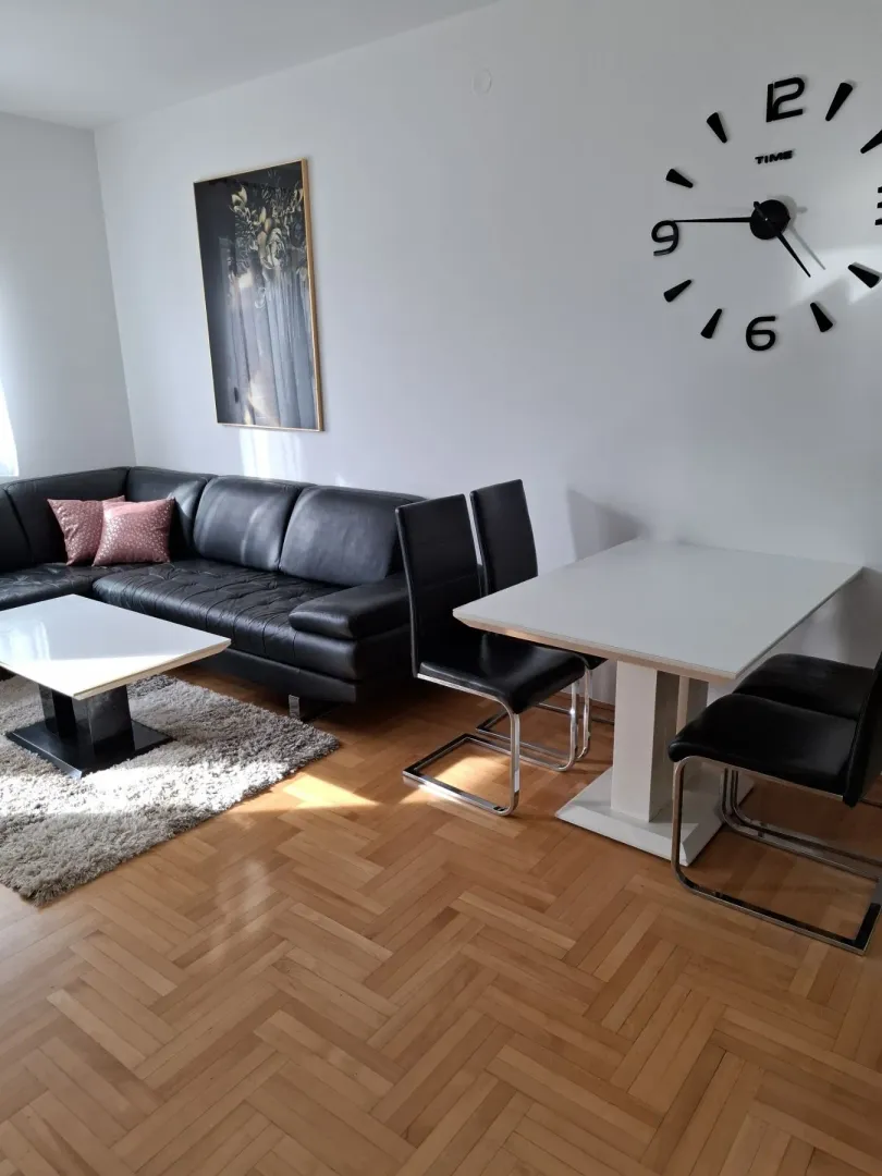 Bright living room featuring a black leather sofa and a dining table.