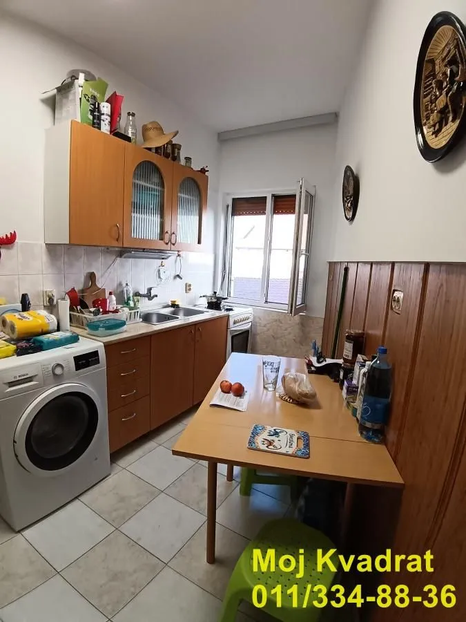 Manja kuhinja sa drvenim elementima, trpezarijskim stolom i ugrađenom mašinom za veš.