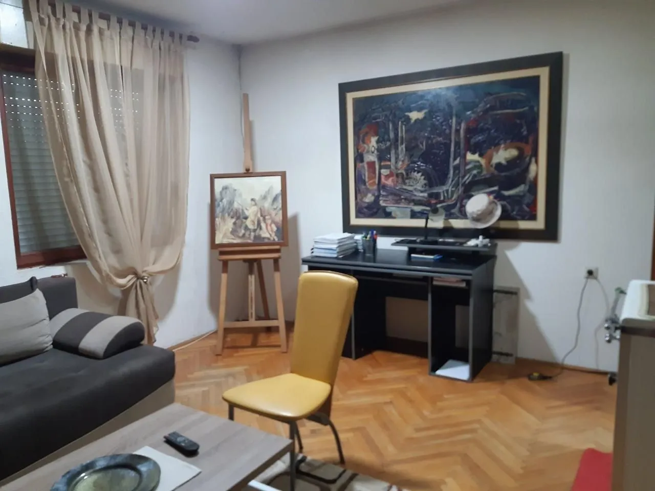 Dnevna soba sa garniturom, radnim stolom i umjetničkim slikama.