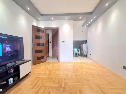 Dnevna soba sa drvenim podom, televizorom i vratima koja vode u hodnik. - image 3