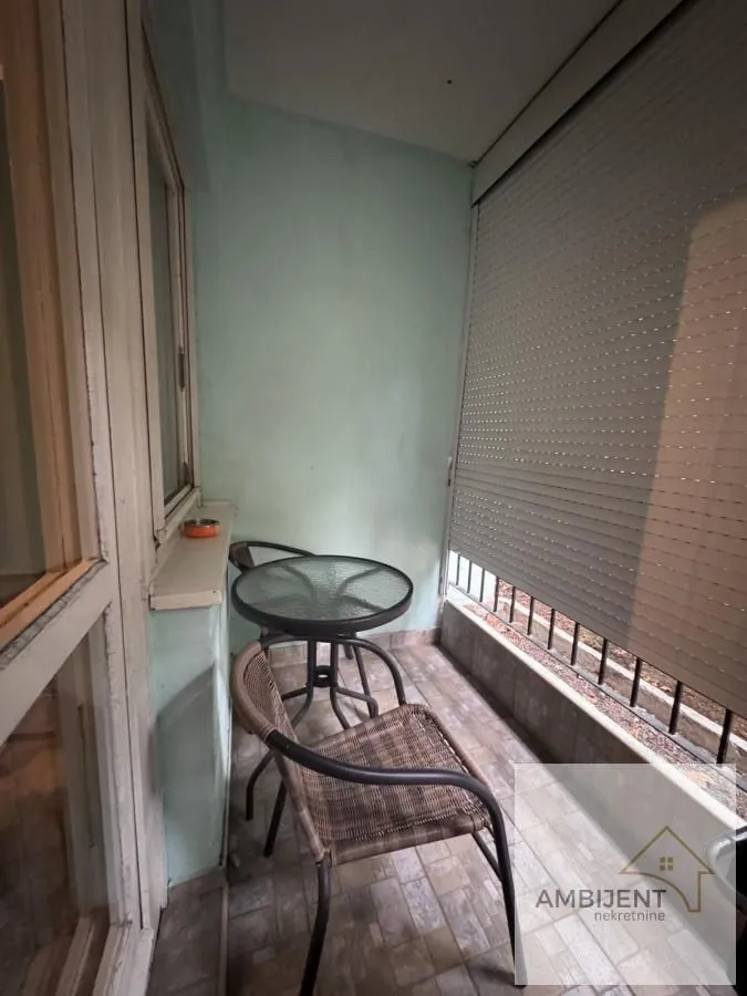 Natkriveni balkon sa garniturom za sedenje i roletnama na prozorima.