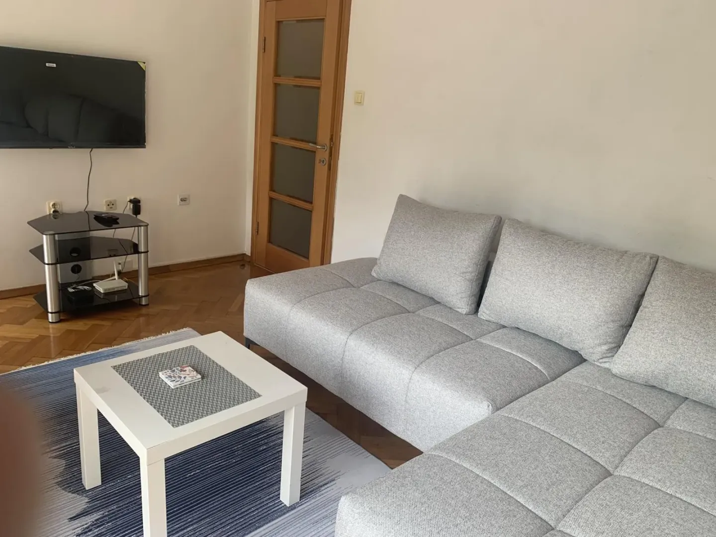 Svijetla dnevna soba sa sivom ugaonom garniturom i klupskim stolom.