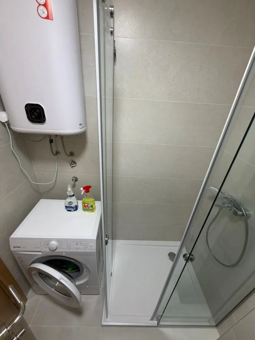 Bathroom with a shower cabin, washing machine, and water heater.