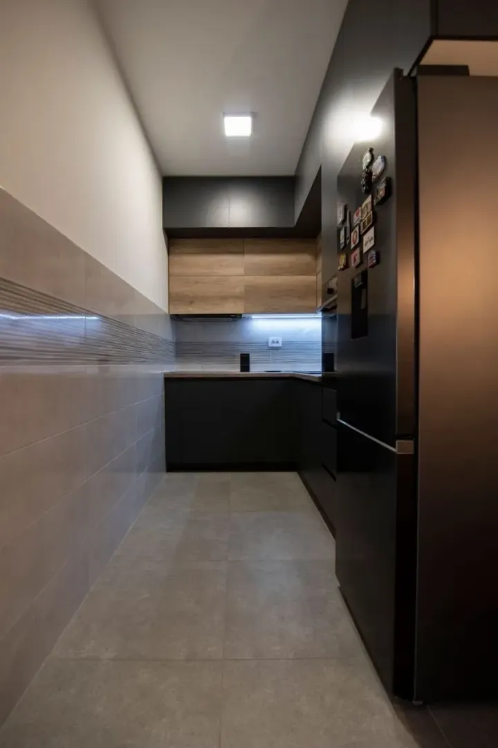 Modern narrow kitchen with dark cabinets and wooden details.