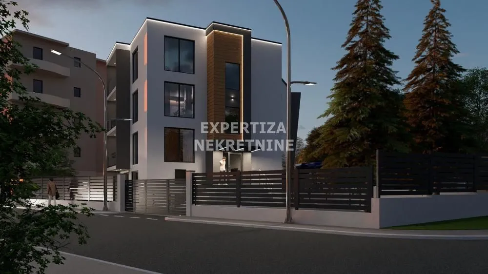 Exterior view of a modern residential building with lighting and a fence.