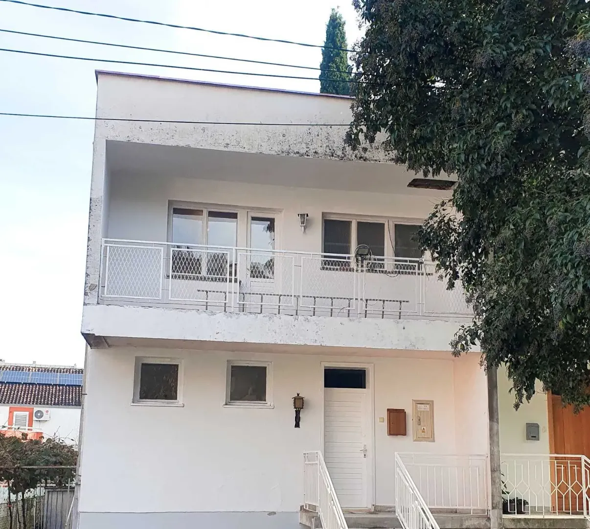 Prednja strana i ulaz dvospratne bijele kuće sa balkonom.