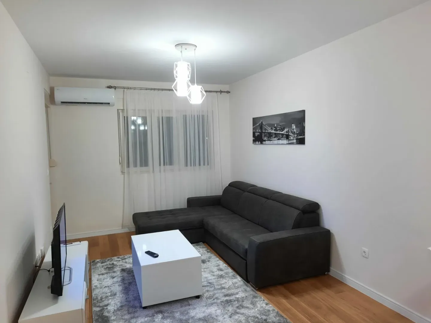 Bright living room featuring a dark corner sofa, a white coffee table, and a TV.