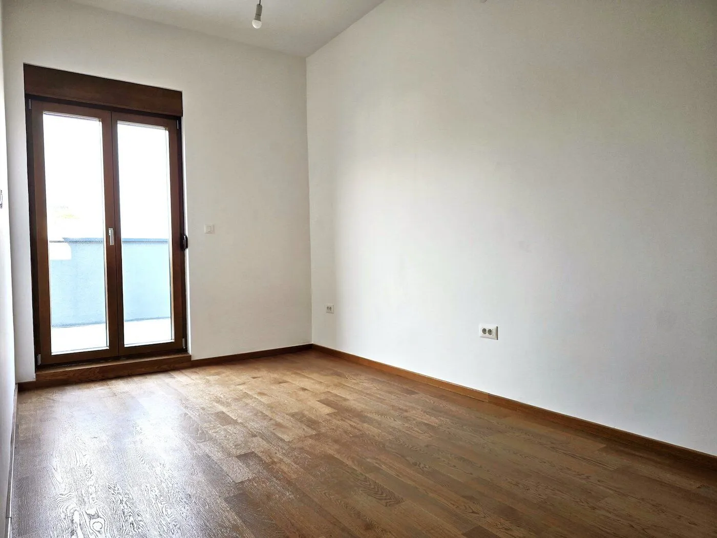 Empty room with hardwood floors and balcony doors.