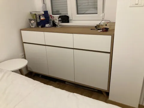 A modern wooden dresser in a bedroom next to the bed. - image 6