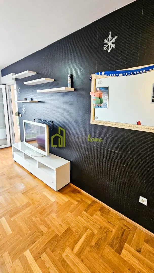 Living room with TV unit, wall shelves, and wooden parquet flooring.
