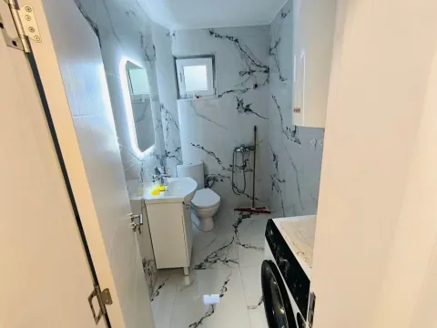 Small bathroom with marble tiles, washbasin, toilet, and washing machine. - image 2