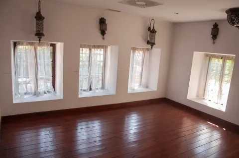 Empty room with wooden flooring, white walls, and small windows. - image 10